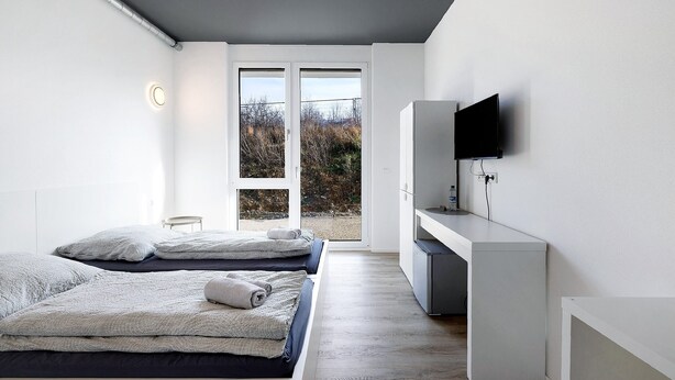 Een moderne slaapkamer met twee bedden, een televisie en een schuifglazen deur naar buiten.