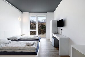 A modern bedroom with two beds, a TV, and a sliding glass door to the outdoors.