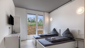 A modern bedroom with two beds, a TV, and a sliding glass door to the outside. - Room '7' with Shared Terrace and Wi-Fi (Dußlingen)