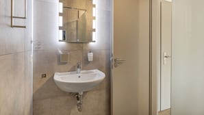 A bathroom with a white sink, a mirror with lights, and a door. - Room '7' with Shared Terrace and Wi-Fi (Dußlingen)