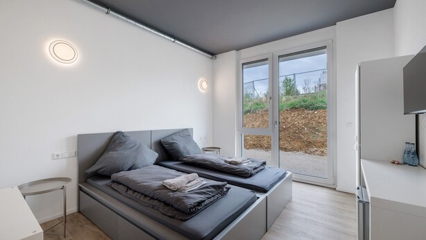 A modern bedroom with a bed, bedside tables, and a view through a glass door. - Room '8' with Shared Terrace and Wi-Fi (Dußlingen)