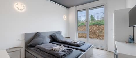 A modern bedroom with a bed, bedside tables, and a view through a glass door.