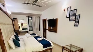 A hotel room with a bed, a TV mounted on the wall, a small table, and a green sofa. - My Home Hotels (New Delhi)