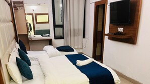 A neatly made bed with a wooden frame, a green upholstered bench, and a television mounted on the wall. - My Home Hotels (New Delhi)