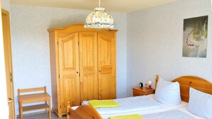 A bedroom with a wooden wardrobe, a bed with pillows, a bedside table with a lamp, and a chair. - Apartment '1, 53qm, Balkon' with Shared Pool, Shared Terrace and Wi-Fi (Wasserburg (Bodensee))
