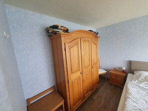 A bedroom with a wooden wardrobe, a wooden nightstand, a bedside table, a bed, and a chair. - Apartment '1, 53qm, Balkon' with Shared Pool, Shared Terrace and Wi-Fi (Wasserburg (Bodensee))