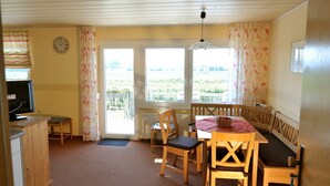 A room with a dining table, chairs, a television, and a view of a green landscape through the windows. - Apartment '1, 53qm, Balkon' with Shared Pool, Shared Terrace and Wi-Fi (Wasserburg (Bodensee))