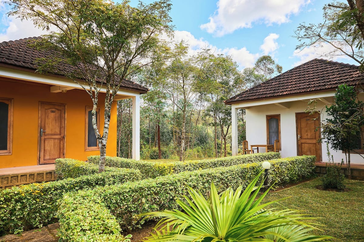 Two yellow buildings with wooden doors, surrounded by well-maintained hedges and trees.