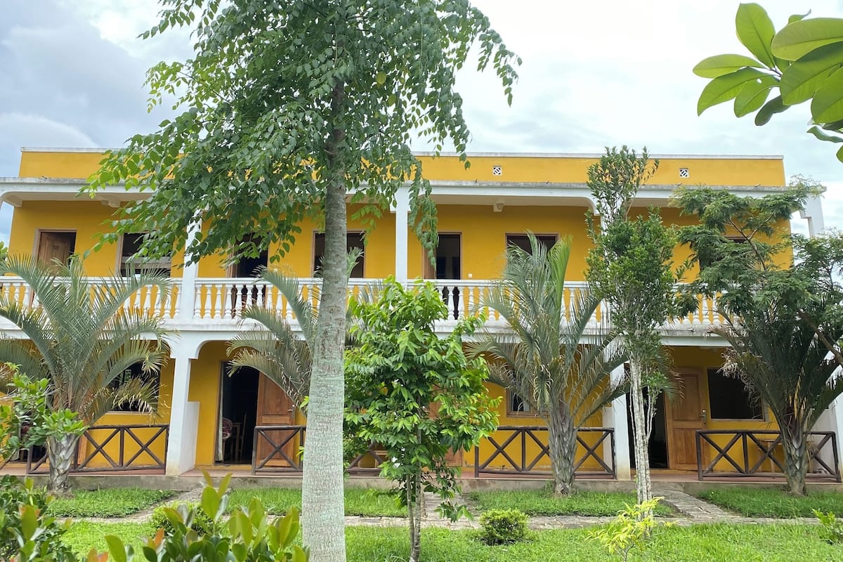 A yellow building with a balcony and a tree in the foreground.