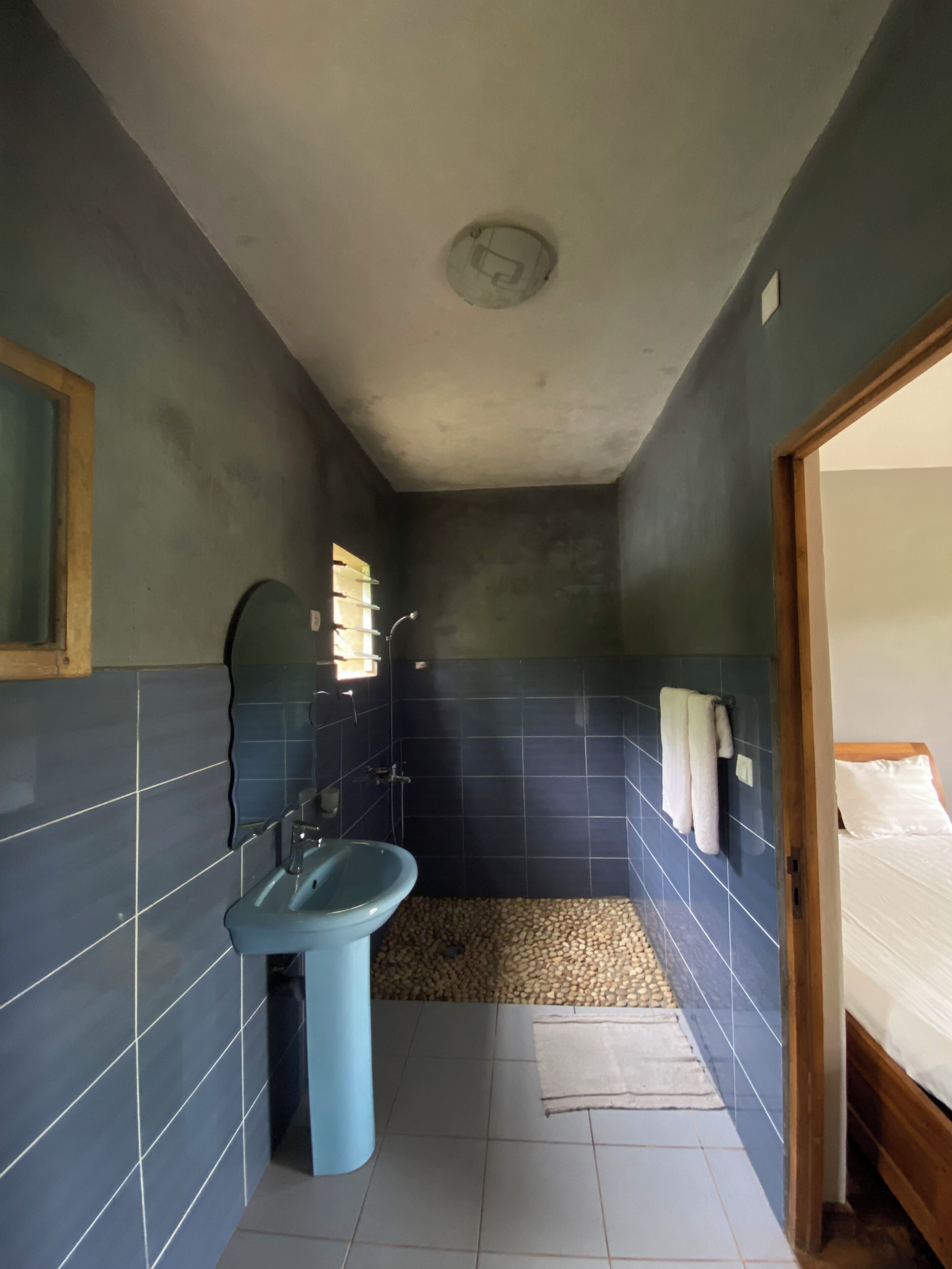A narrow bathroom with a blue sink, a shower, and a small window.