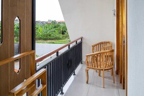A balcony with a wooden chair, a metal railing, and a view of greenery and buildings.