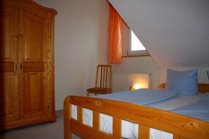 Un dormitorio con una cama de madera, una silla, un armario y una ventana con cortinas.