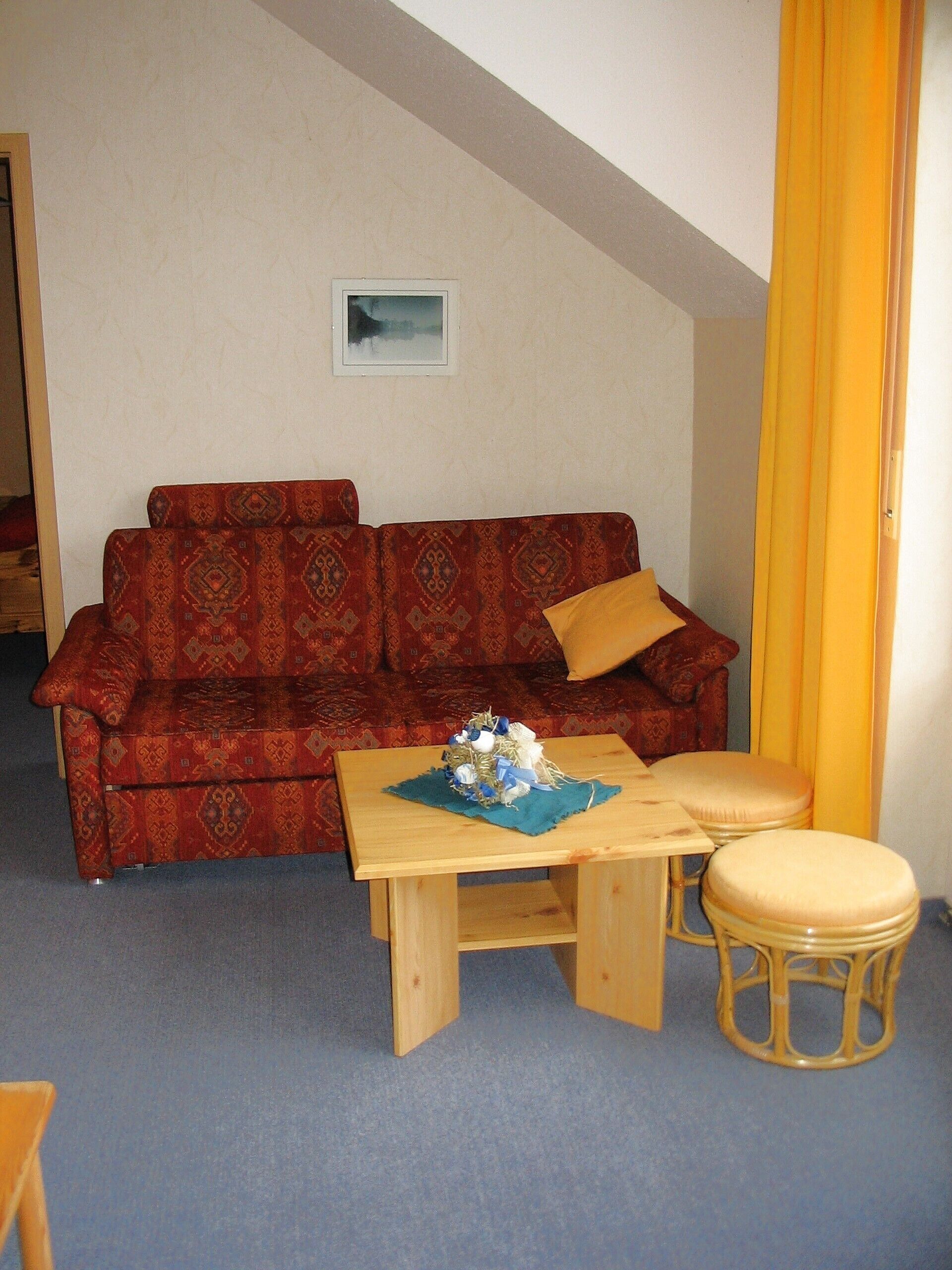 A living room with a red patterned sofa, a wooden coffee table, and a yellow curtain.