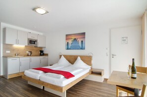A modern hotel room with a bed, a dining table, a kitchen area, and a painting on the wall. - Apartment 'Apt Typ A1' with Shared Terrace, Shared Garden and Wi-Fi (Immenstaad am Bodensee)
