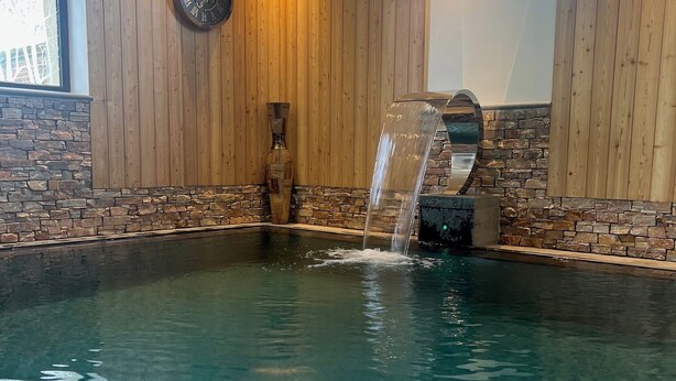 A spa pool with a waterfall feature, wooden walls, and a stone accent wall. - Le Domaine Des Fagnes (Sains-du-Nord)