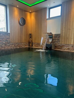 Een wellnessbad met een waterval, houten wanden en een accentmuur van steen.