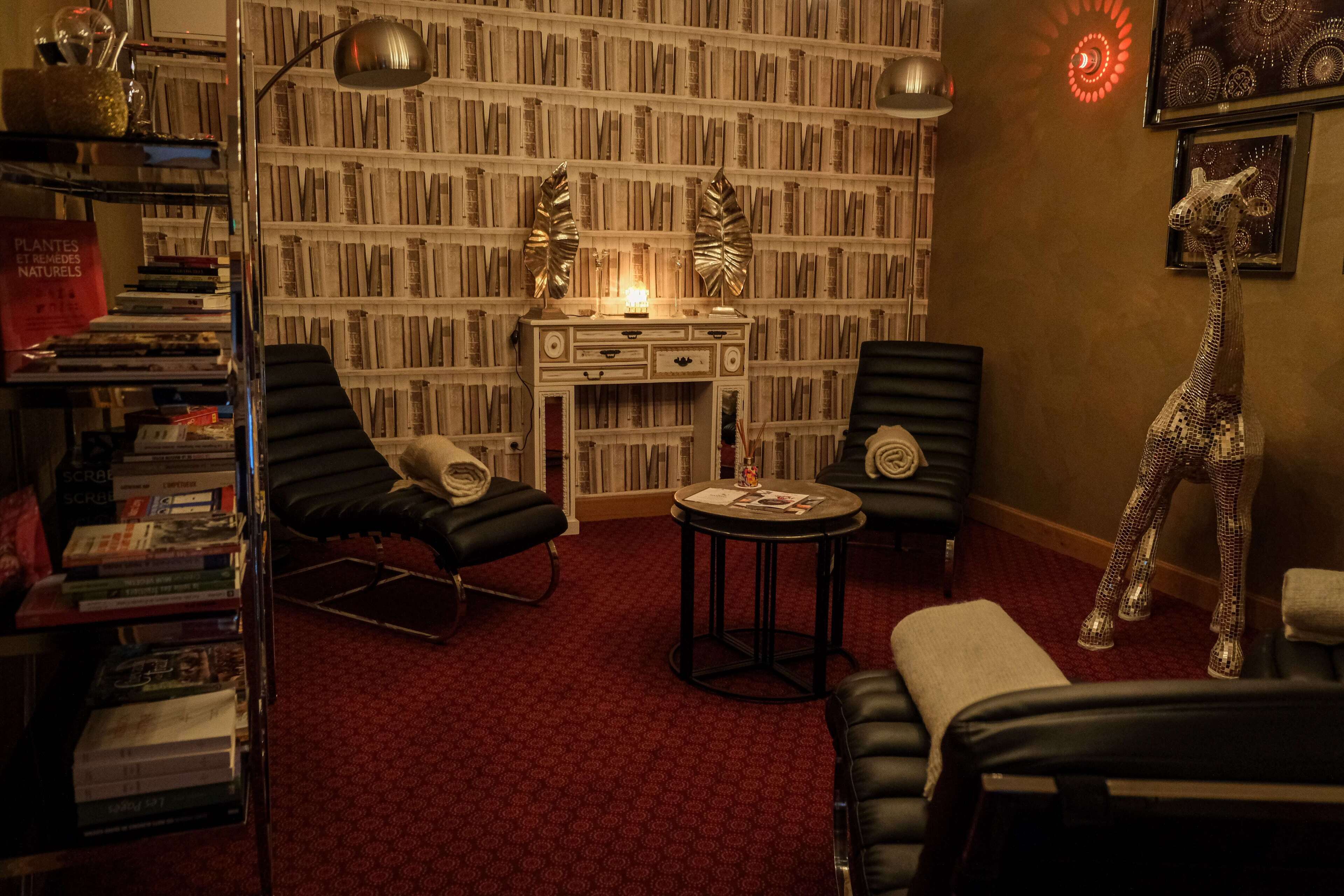 A library with bookshelves, two black leather chairs, a small round table, and a giraffe sculpture.
