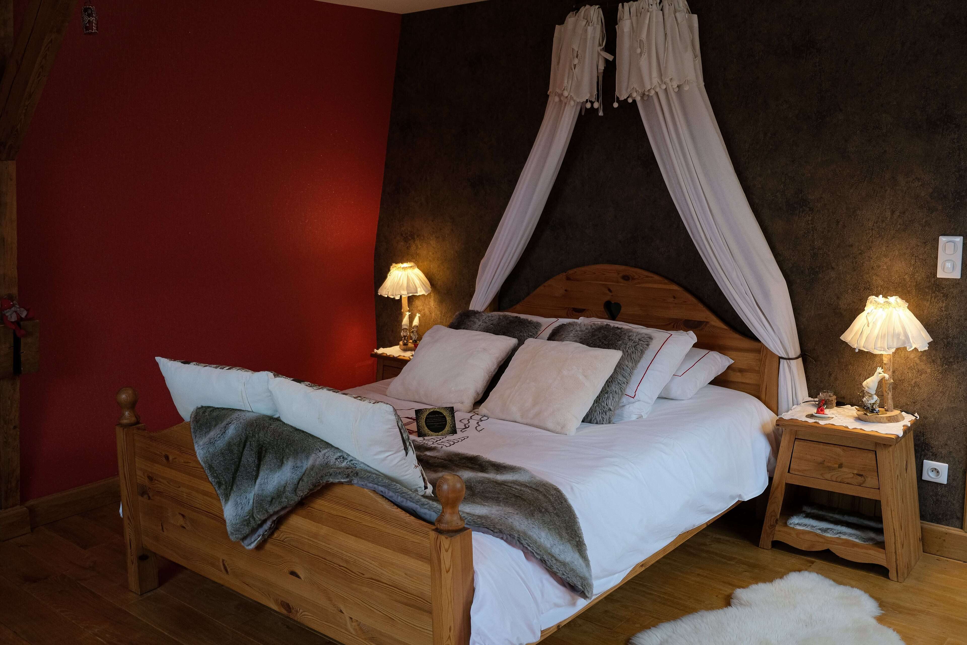 Una cama de madera con dosel, mesitas de noche con lámparas y una pared de acento roja.