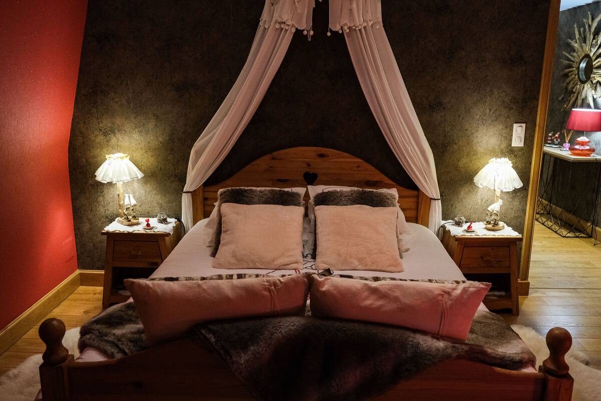 Un dormitorio con cama con dosel, dos mesitas de noche con lámparas y un espejo en la pared.
