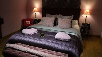 Una cama bien hecha con una colcha estampada, dos lámparas de noche, una silla roja y un banco.