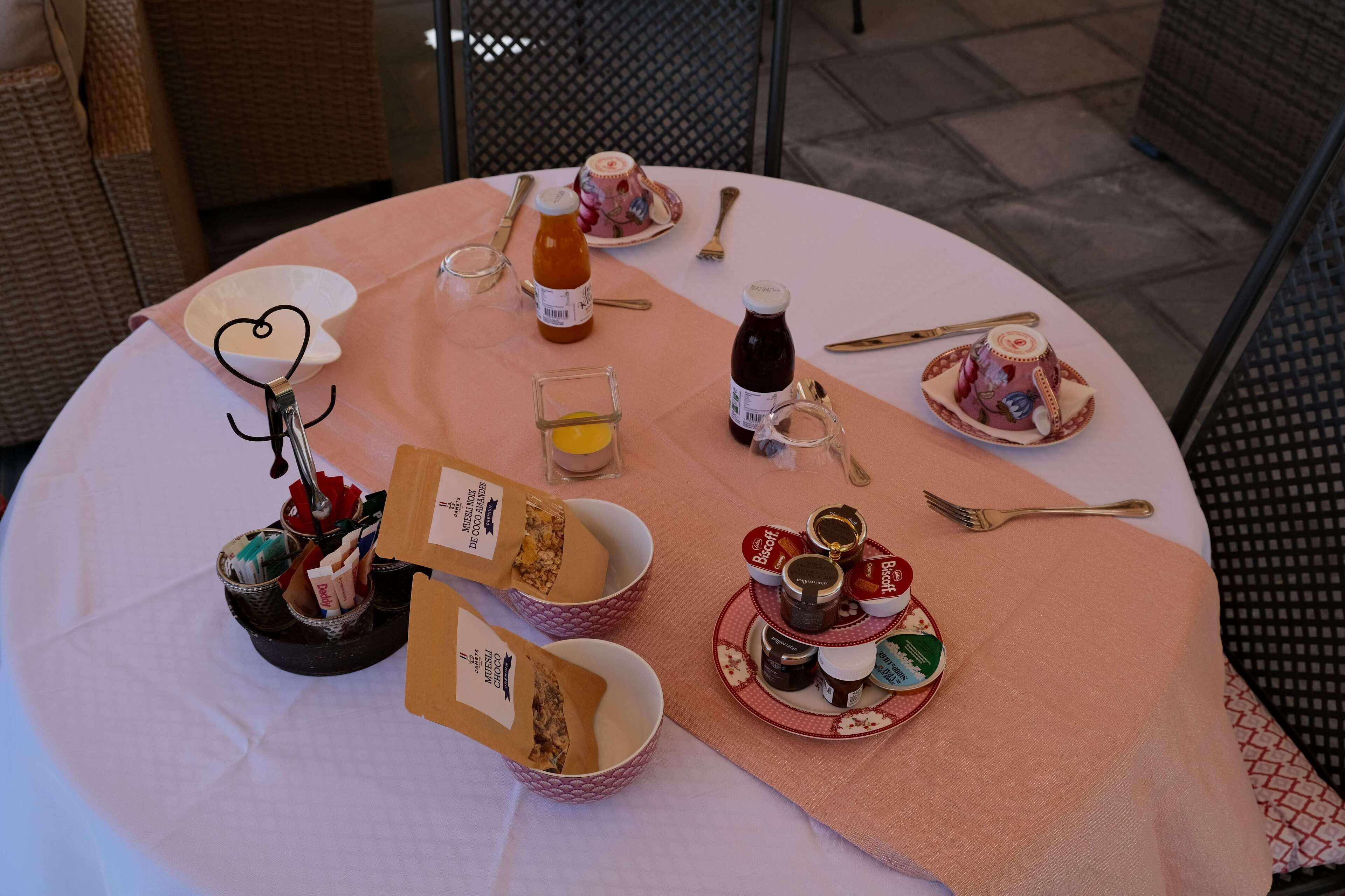 Una mesa redonda con mantel rosa, diversos alimentos, condimentos y utensilios.