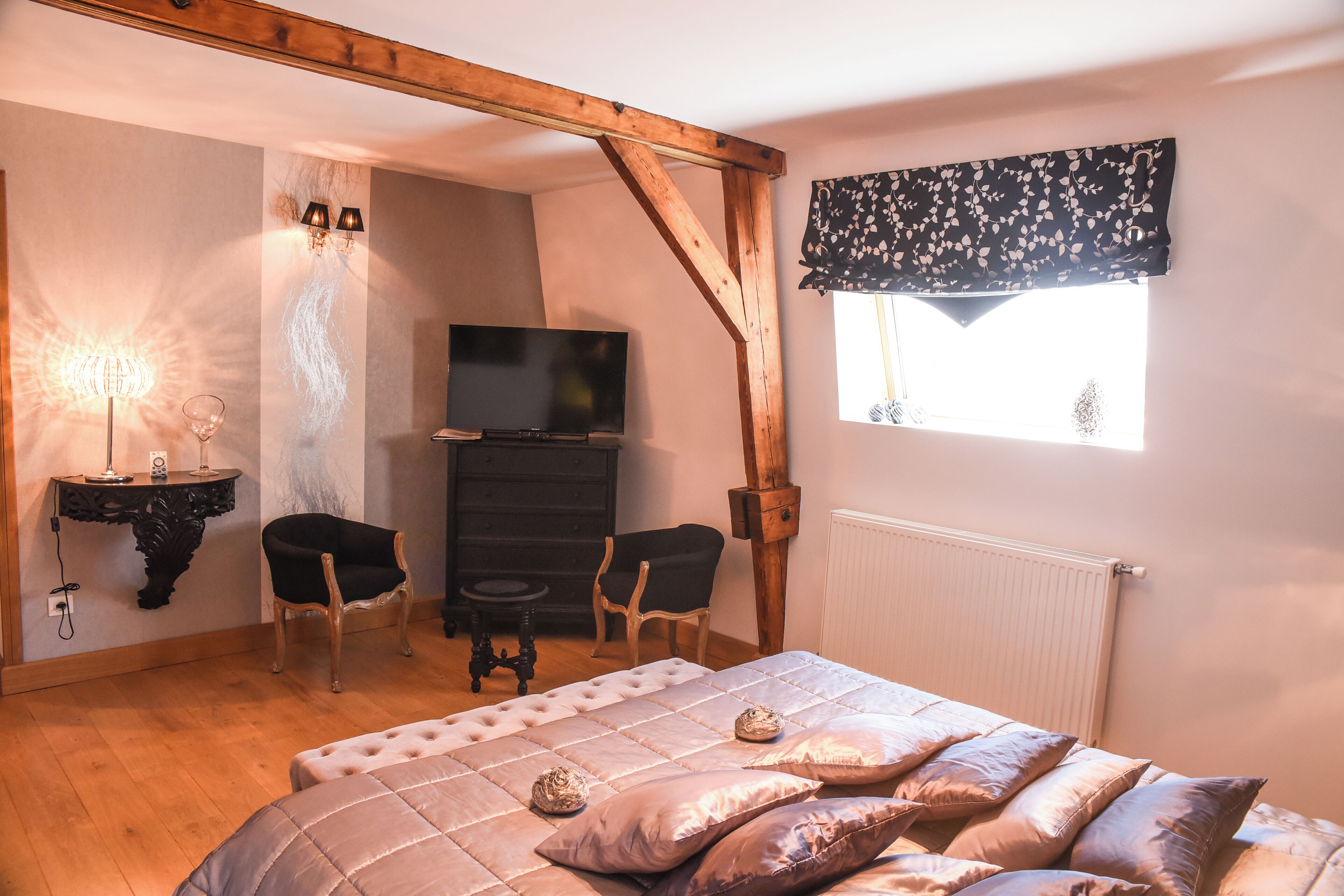Ein Schlafzimmer mit einem Bett, zwei Stühlen, einem Fernseher, einer Lampe und einem Fenster mit Vorhang.