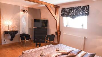 Ein Schlafzimmer mit einem Bett, zwei Stühlen, einem Fernseher, einer Lampe und einem Fenster mit Vorhang.