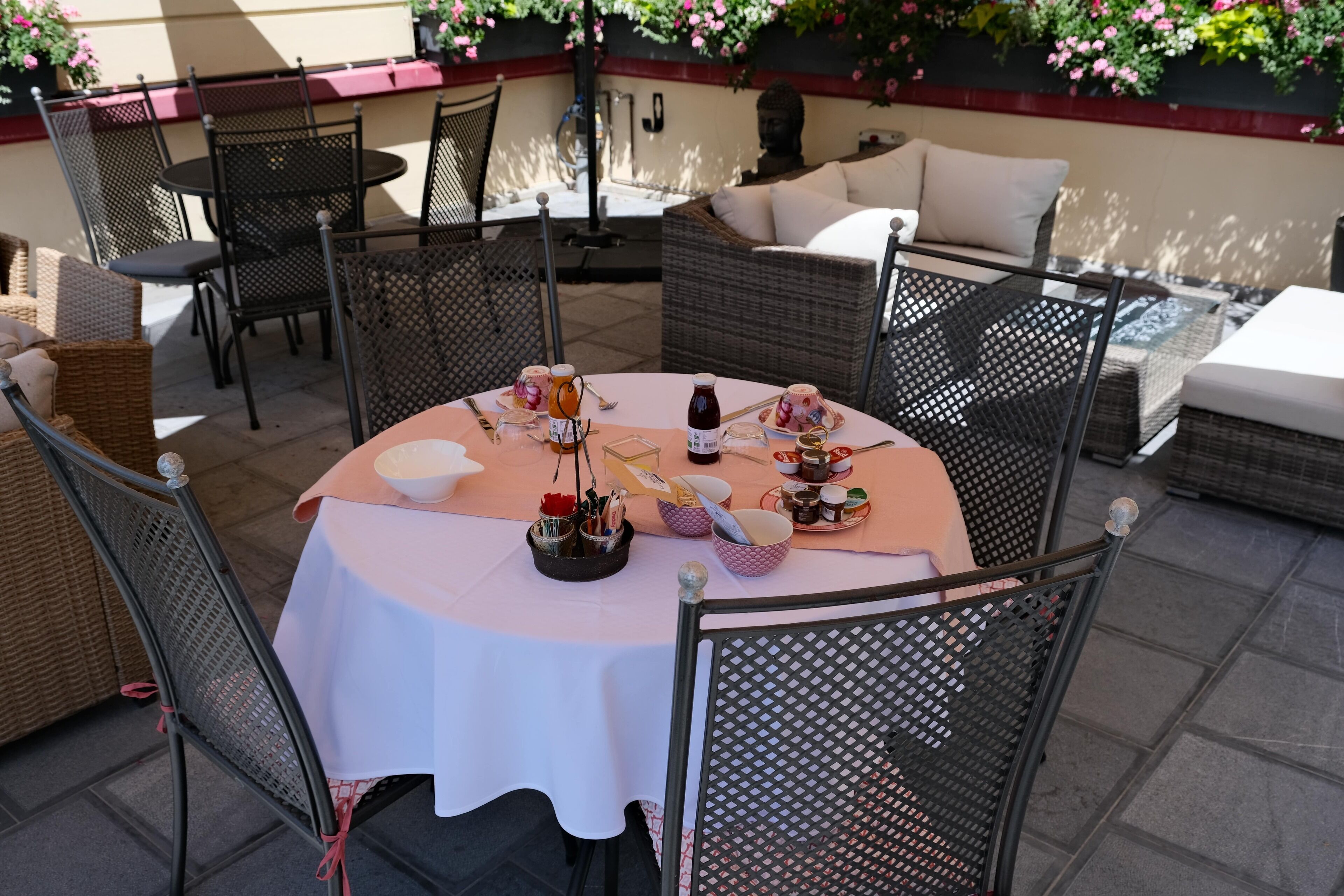 An outdoor patio with wicker furniture, a round table with a white tablecloth, and a variety of condiments and utensils.
