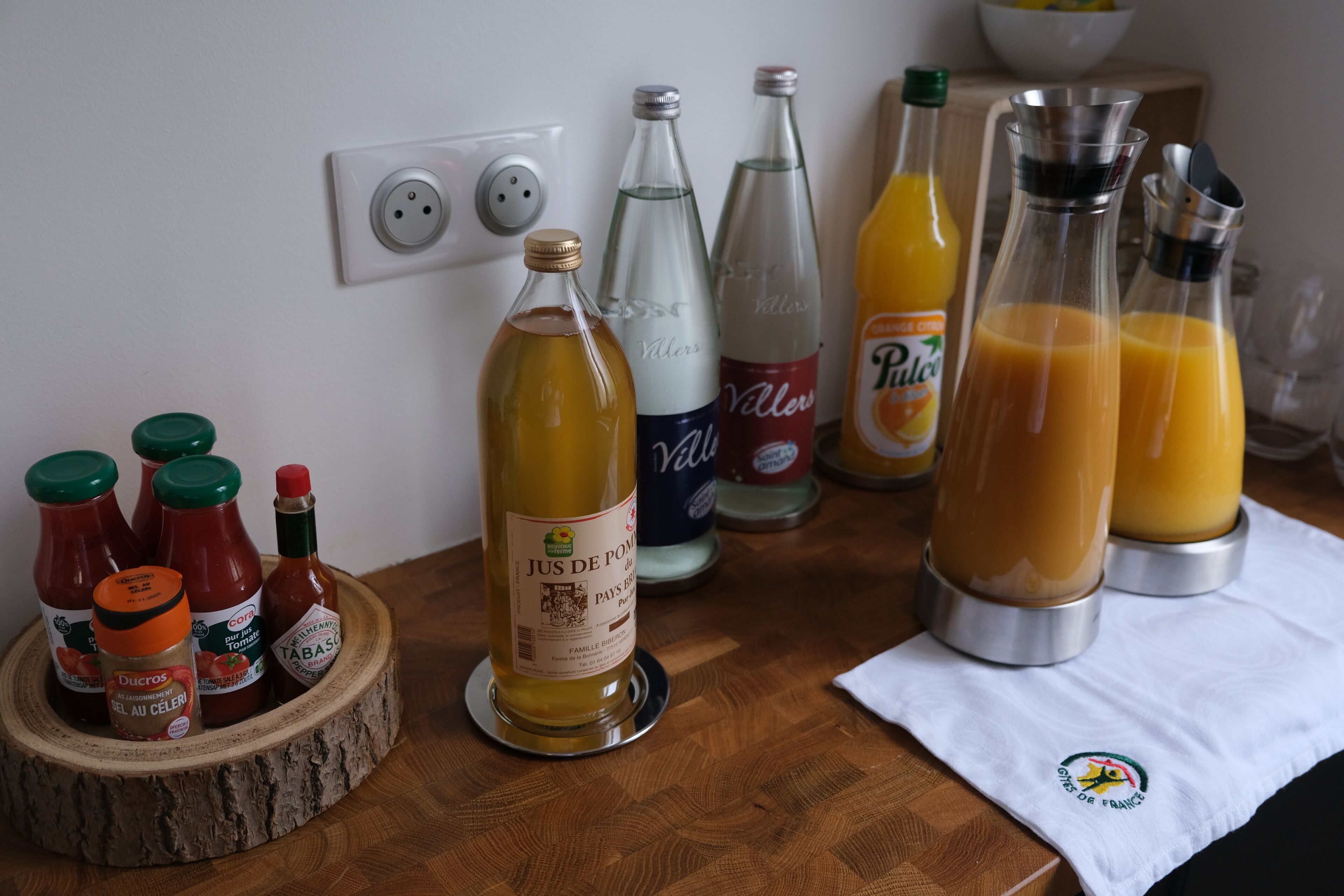 A wooden table with various bottles of condiments and beverages, including ketchup, mustard, and orange juice.