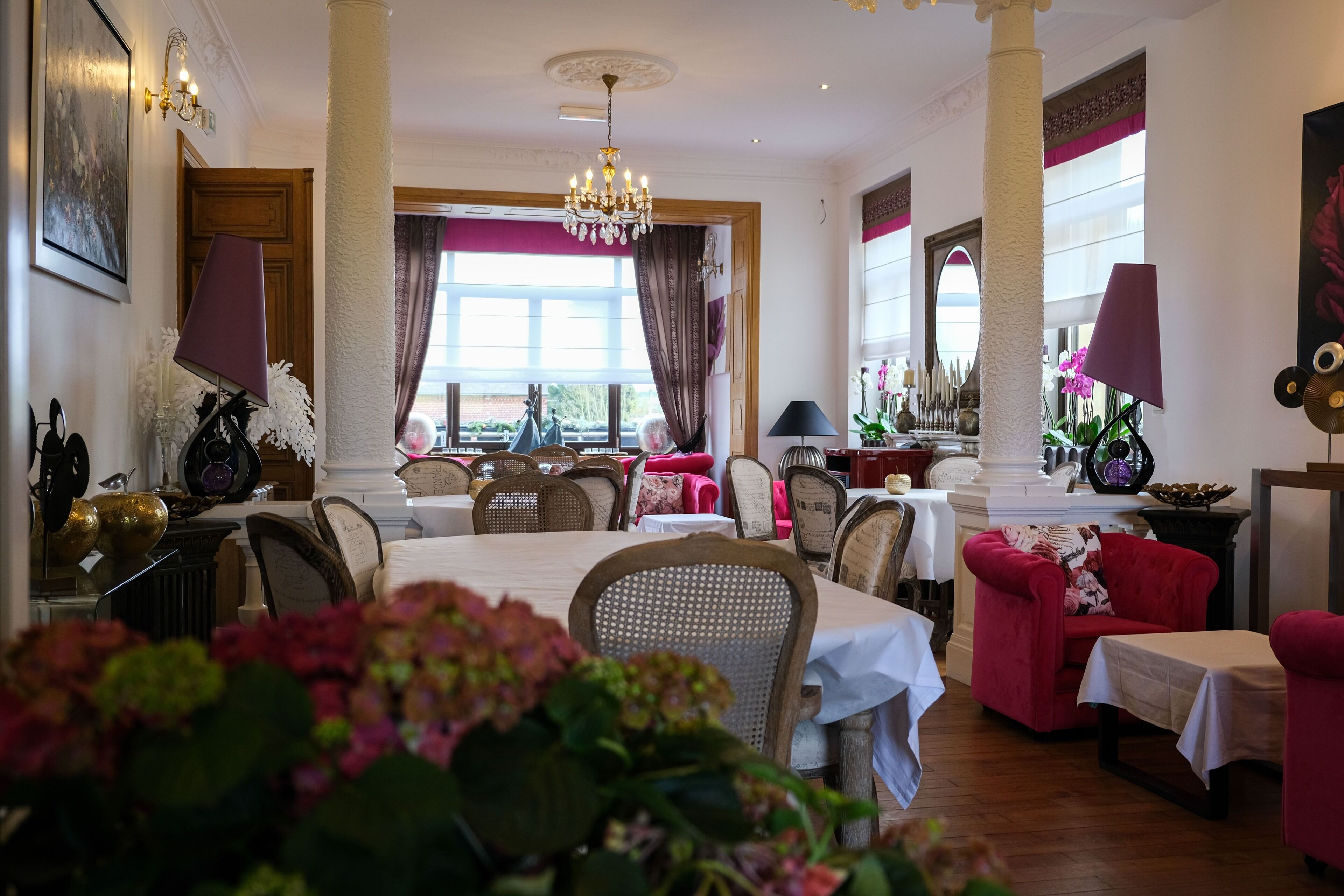 Un espace repas avec des tables et des chaises, un lustre et une vue dégagée sur l’extérieur grâce à de grandes fenêtres.