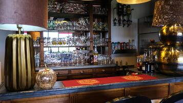 Zona de bar con estantes de cristalería y botellas, mostrador de madera y posavasos rojo.