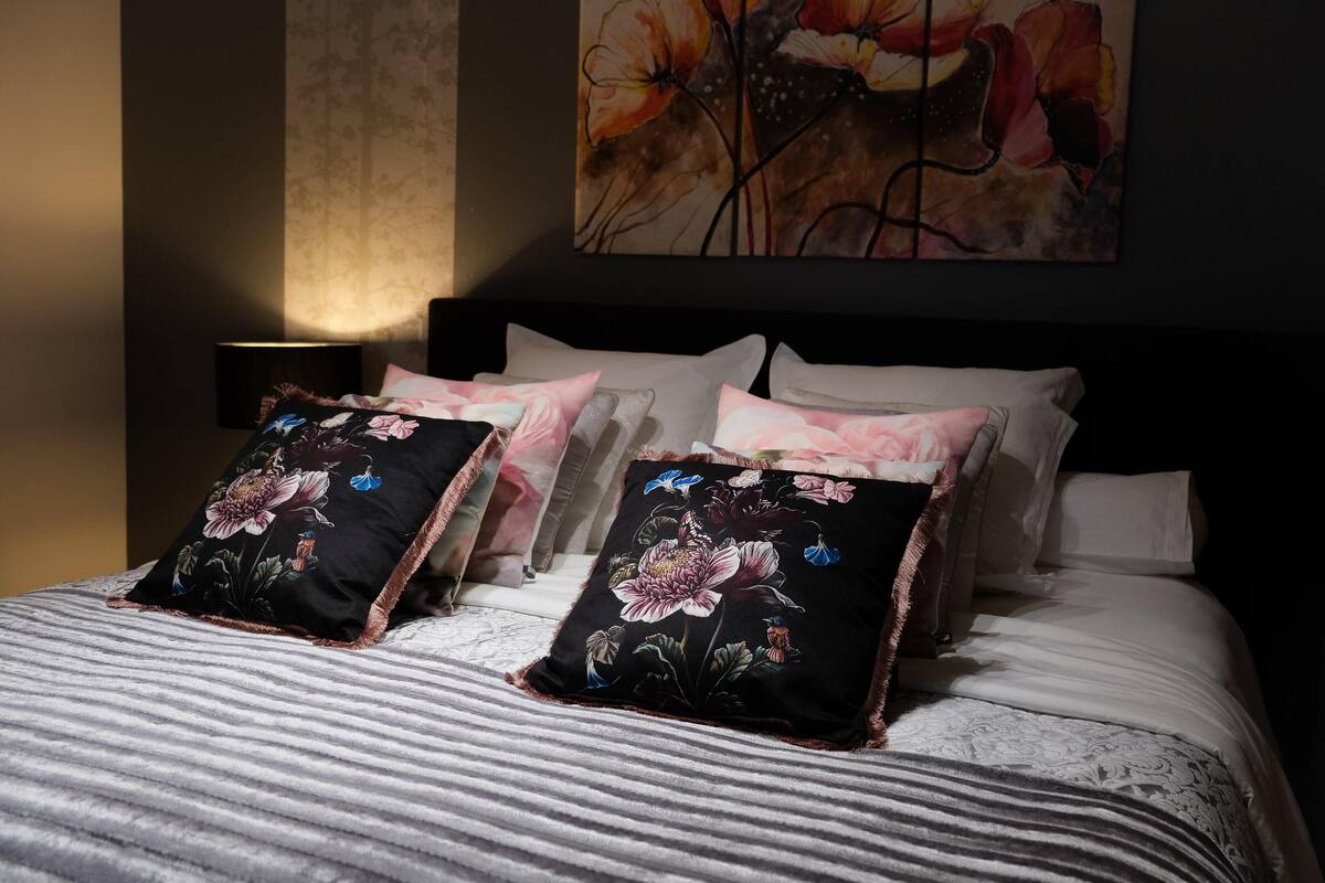 Una cama bien hecha con almohadas estampadas con flores y una manta a rayas.