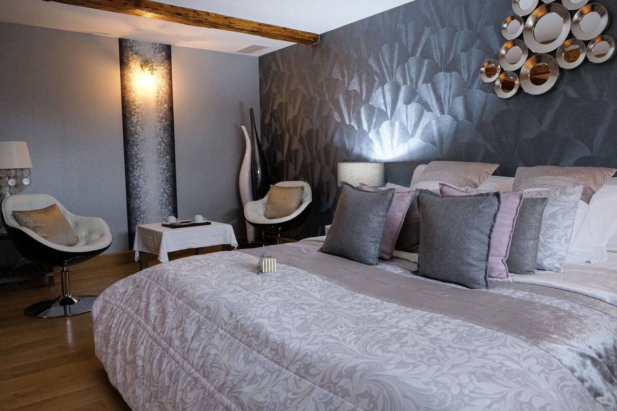 Un dormitorio moderno con una cama grande, una silla, una mesita de noche y un espejo montado en la pared.