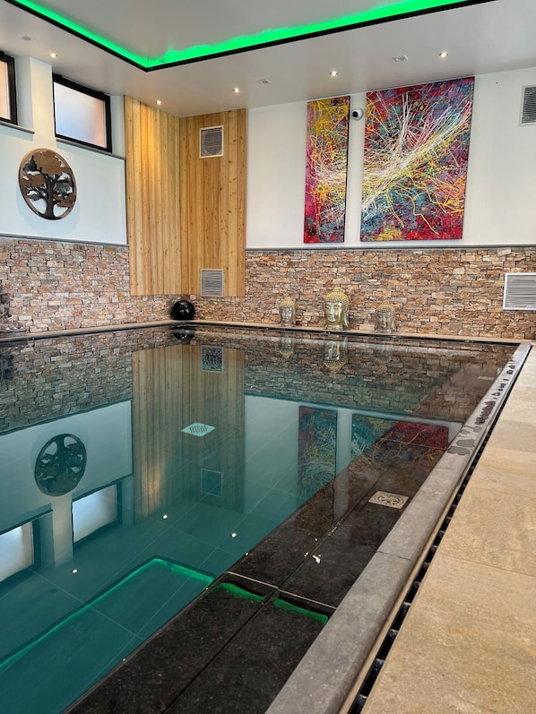 Piscina interior moderna con pared de piedra y detalles de madera, que presenta una gran estatua de Buda y arte abstracto.
