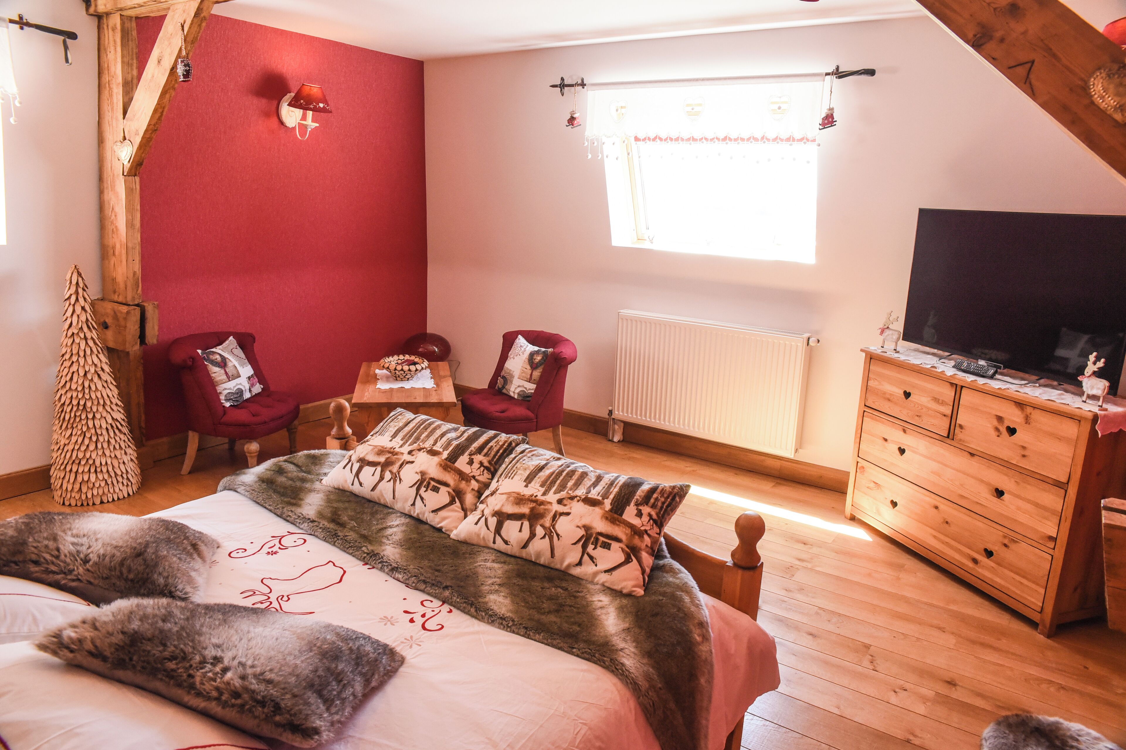 A bedroom with a bed, a wooden dresser, a television, and a window with curtains.