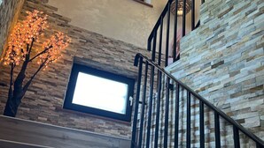 A staircase with stone walls, a wooden handrail, and hanging pendant lights. - Le Domaine Des Fagnes (Sains-du-Nord)
