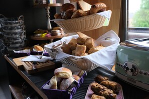 Ein reichhaltiges Frühstücksbuffet mit verschiedenen Backwaren, darunter Brot und Gebäck, präsentiert auf einem Tisch mit einem Vintage-Toaster.