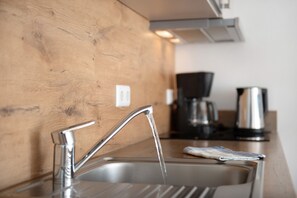A kitchen with a stainless steel sink, a wooden wall, and a coffee maker in the background.
