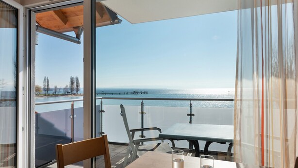A balcony with a table and chairs, a glass railing, and a view of the sea. - Apartment 'Apt Typ A1 21' with Shared Terrace, Shared Garden and Wi-Fi (Immenstaad am Bodensee)