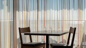 A dining area with a table and chairs, a view through sheer curtains, and a glass on the table. - Apartment 'Apt Typ A1 21' with Shared Terrace, Shared Garden and Wi-Fi (Immenstaad am Bodensee)