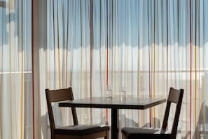 Un comedor con una mesa y sillas, vistas a través de cortinas traslúcidas, y un vaso sobre la mesa.