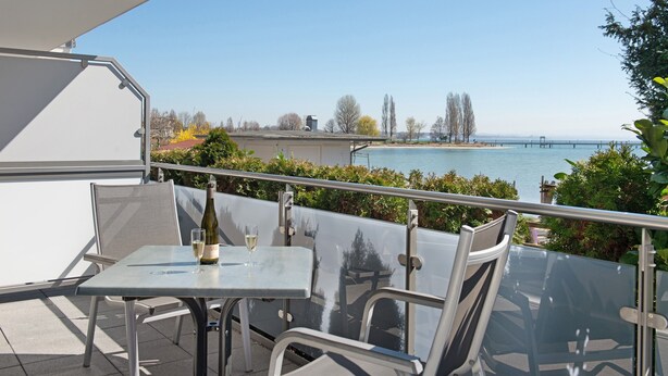 A balcony with a table and chairs, overlooking a body of water and a bridge. - Apartment 'A1' with Shared Terrace, Shared Garden and Wi-Fi (Immenstaad am Bodensee)