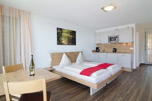 Una habitación de hotel moderna con una cama de madera, una mesa de comedor, una zona de cocina y un cuadro en la pared.