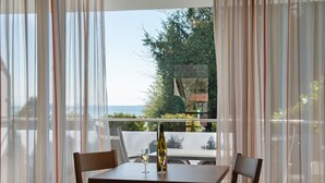 Ein Tisch mit Flasche und Glas, Vorhänge und Blick auf Meer und Grünflächen.