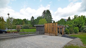 Un espace extérieur aménagé avec une surface pavée, une structure en bois, une voiture et de la végétation environnante.