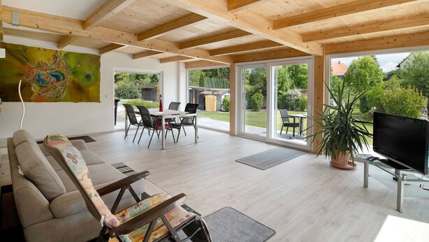 Un grand espace de vie doté d’un plafond en bois, d’un canapé, d’une télévision et d’une table à manger avec des chaises.