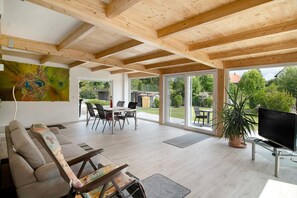 Un grand espace de vie doté d’un plafond en bois, d’un canapé, d’une télévision et d’une table à manger avec des chaises.