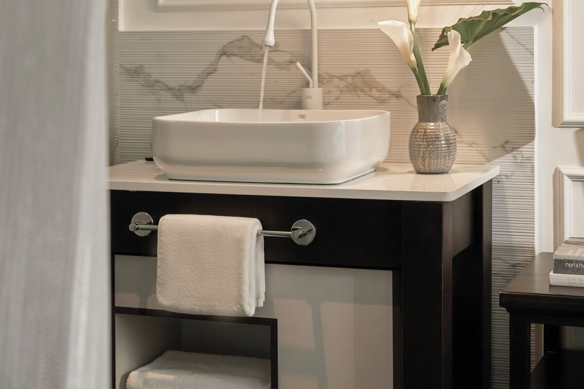 A modern bathroom with a white sink, a round mirror, and a hanging light fixture.