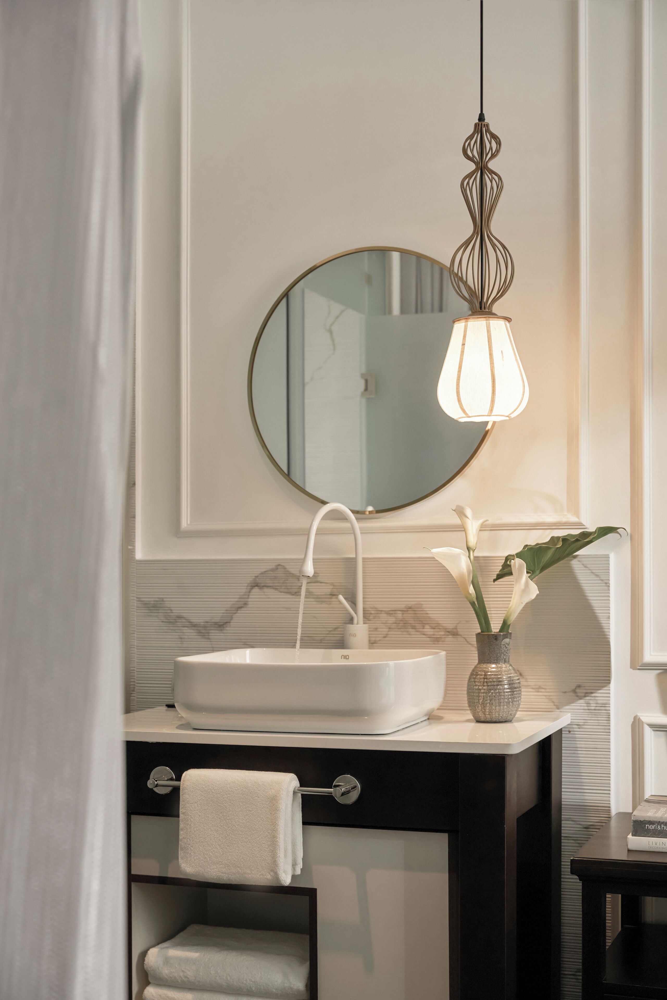 A modern bathroom with a white sink, a round mirror, and a hanging light fixture.