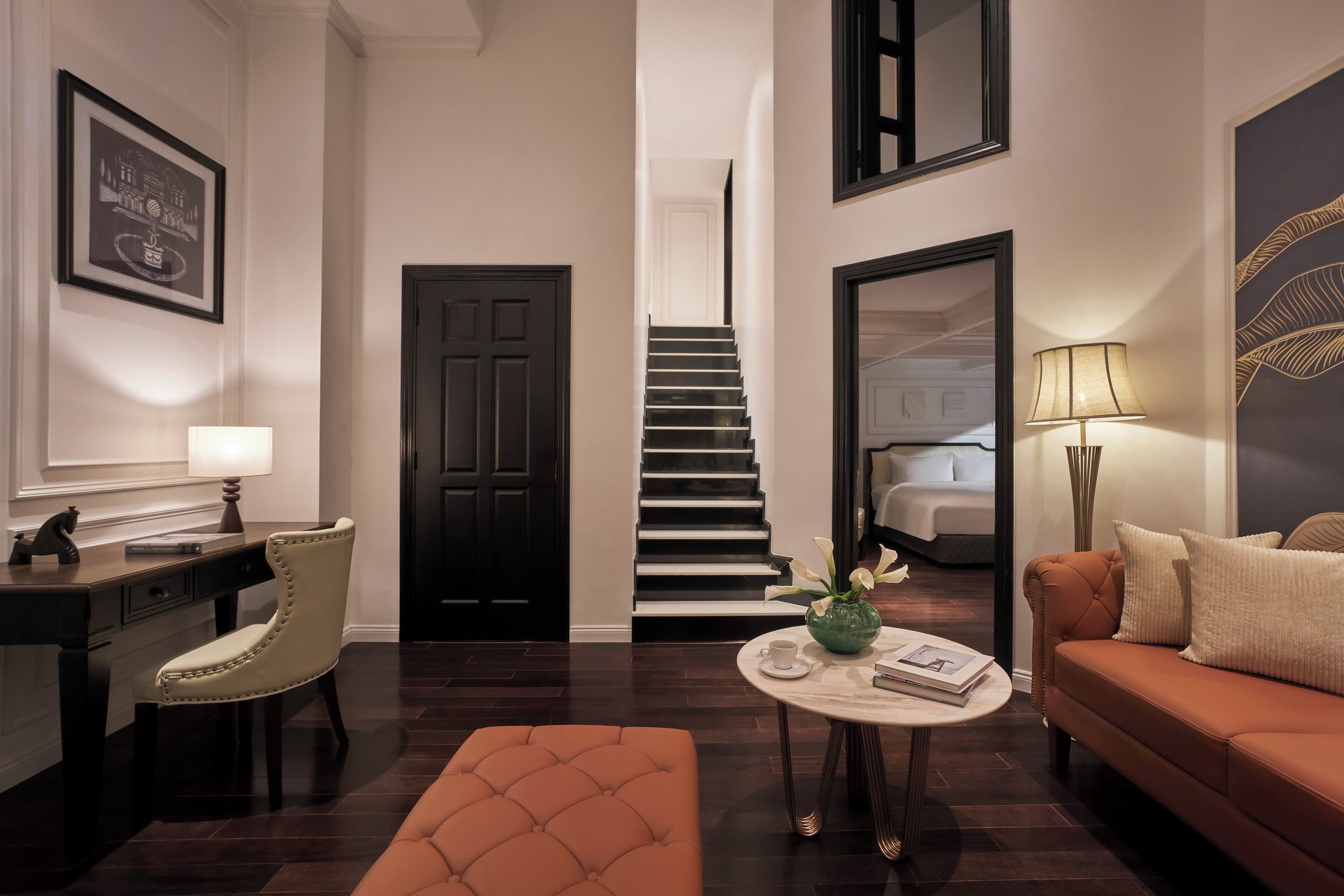 Un salon moderne comprenant un canapé, une table basse, un bureau et une chaise. Un escalier mène à une autre pièce.